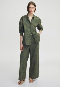 Olijfgroene shirt en wijde broek set, met bloemdessin en uitsnijdingen. Lichtgewicht stof met een ontspannen pasvorm.