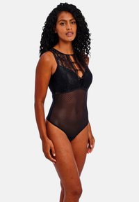 Bodysuit negro con detalles de encaje en la parte superior, una sección inferior de malla con un patrón de puntos y una forma ajustada. Acentuado con elementos metálicos.