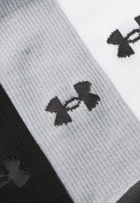 Three pairs of socks in black, grey, and white, featuring a prominent black logo. The fabric is ribbed with a medium thickness.