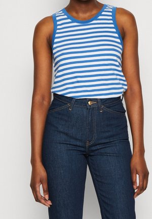 Frau trägt blau-weißen, horizontal gestreiften, ärmellosen Top, in hoch taillierte dunkelblaue Jeans gesteckt.