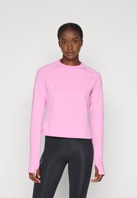 Maglietta sportiva a maniche lunghe di colore rosa chiaro con una texture a coste e maniche raglan, abbinata a leggins neri. Design semplice, senza loghi visibili.