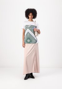 T-shirt blanc avec un panneau à motifs verts, associé à une jupe rose pâle longueur genoux avec des boutons sur le devant et des bottines noires.