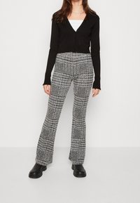 Czarny krótki kardigan z zapięciem na guziki w zestawieniu z wysokim stanem, teksturowanymi spodniami w deseń houndstooth w czerni i bieli, noszonymi z czarnymi botkami.