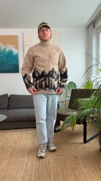 Beige fleece pull-over met berg- en bosprint in zwart, een halve ritssluiting aan de voorkant en een borstzak. Gecombineerd met lichtblauwe jeans en sneakers.