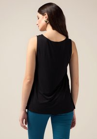 Top senza maniche nero con una vestibilità rilassata, texture liscia e scollo rotondo. Indossato con pantaloni turchesi e accessoriato con orecchini d'oro.