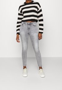 Černobílý pruhovaný krátký pletený svetr s dlouhými rukávy, kombinovaný se světle šedými úzkými džínami s vysokým pasem a bílými teniskami.