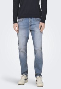 Světle modré džíny z denimu se stahovaným střihem, se zesvětlenými oblastmi a klasickým designem pěti kapes. V páru s bílými teniskami.