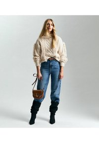 Suéter de punto crema con detalles texturizados, jeans azul de tiro alto, botas holgadas negras y un bolso bandolera marrón.