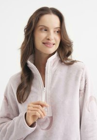 Sudadera de forro polar rosa claro con un cuello de cremallera de un cuarto, que presenta una textura suave y patrones de luna creciente en la tela.