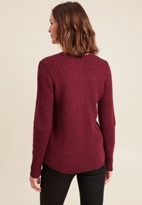 Maglione a maglia bordeaux con una trama a coste, maniche lunghe e orlo arrotondato. Presenta una vestibilità rilassata con leggere aperture sui lati.