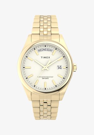 Montre-bracelet Timex en doré avec un cadran blanc, indication du jour et de la date, bracelet en acier inoxydable, et marqueurs et aiguilles luminescents. Résistante à l'eau jusqu'à 5 ATM.