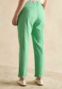 Rohelised puuvillased püksid lõdva lõikega, millel on sisse rullitud äär ja tagataskud, mida täiendavad istuva elastse vöökohaga.