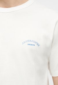 Λευκό μπλουζάκι με λαιμόκοψη crew και ανοιχτό γαλάζιο κείμενο "JACK & JONES ARCHIVE" εκτυπωμένο στο αριστερό στήθος.