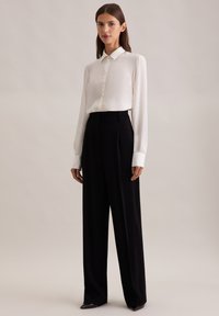 Biała koszula z długim rękawem i kołnierzykiem, zestawiona z czarnymi, wysokimi spodniami w kant o gładkiej teksturze.