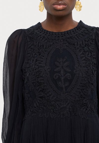 Black dress featuring intricate lace embroidery with floral patterns, sheer puff sleeves, and a round neckline. Textured fabric detail present.