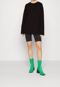 Musta pitkähihaista puseroa on yhdistetty harmaisiin pyöräilyshortseihin, ja asusteena ovat vihreät lakatut nilkkasaappaat, joissa on paksut korot ja krokotiilikuosi.