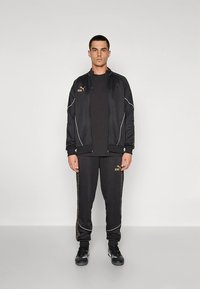 Black athletic tracksuit featuring a zip-up jacket with white piping and a matching pair of pants with gold accents and logos.