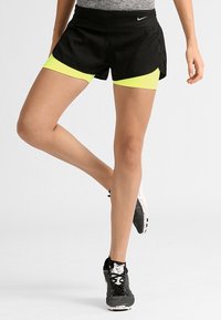 Pantalones cortos deportivos negros con una cintura ancha, que presentan pantalones internos de color amarillo brillante. La tela es ligera y tiene una textura suave.
