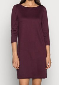 Robe bordeaux longueur genoux en tissu lisse, dotée d'un col rond et de manches trois-quarts. Design simple et ajusté.