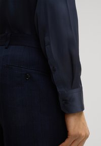 Chemise en satin bleu marine au design épuré, avec des manches longues et des poignets à boutons, associée à un pantalon bleu marine à rayures fines.