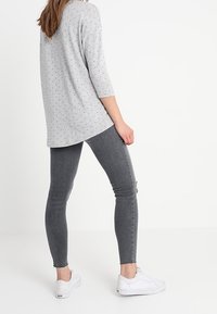 Grå långärmad skjorta med små blommönster, matchad med grå skinny jeans. Modellen bär vita sneakers, vilket ger en avslappnad outfit.