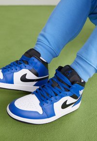 Höga sneakers med vit bas, blå läderdetaljer, svart swoosh och svart/blå detaljer. Texturerat läder med rund snörning.