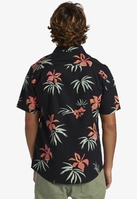 Chemise à manches courtes en tissu noir avec un motif floral tropical aux feuilles roses et vertes. Ourlet arrondi et coupe décontractée.