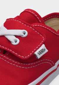 Baskets Vans en toile rouge avec coutures blanches, lacets blancs partiellement noués, et étiquette du logo Vans visible sur le côté près des œillets.