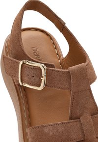 Brown suede wedge sandal with gold buckle, cushioned insole, and stitched edges, showing ankle strap and part of the sole.