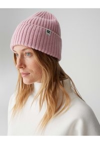 Bonnet rose tricoté avec une texture côtelée et un bord replié, arborant une petite étiquette blanche avec un détail de logo.