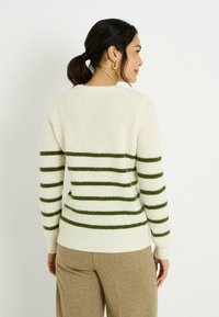 Suéter de punto color crema con franjas horizontales verdes, textura acanalada y ajuste holgado. La parte trasera muestra un cuello redondo y mangas largas.