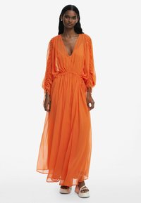 Maxiklänning i livlig orange chiffon, med djup V-ringning, samlad midja, puffärmar och flödande kjol. Bärs med platåsandaler.