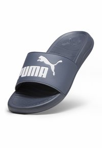 Tamsiai mėlynas šlepetė, pagaminta iš sintetinės medžiagos, su plačia juostele ir balta "PUMA" ženklų, taip pat su tekstūruotu padu, užtikrinančiu sukibimą.