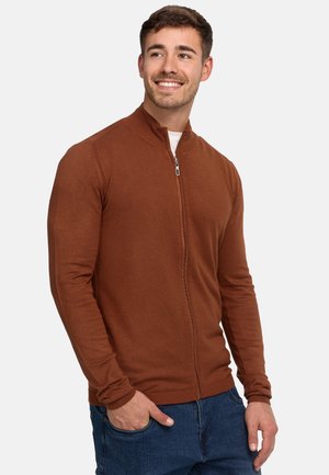 Brun zip-up jakke, ribbet tekstur, stående krave, tætsiddende ærmer, parret med blå jeans. Enkelt design, ingen synlige mønstre eller accenter.