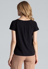Zwarte blouse met korte mouwen en een bootnek, met een plooidetail aan de achterkant en opgerolde mouwen. De stof lijkt glad en lichtgewicht.