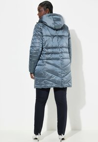 Lichtblauwe pufferjack met capuchon, doorgestikte textuur en een uitlopende pasvorm, gecombineerd met donkere broeken en metallic schoenen.