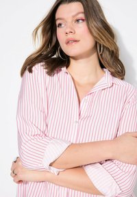 Camisa de botones a rayas en algodón blanco y rosa, con cuello y mangas remangadas, de corte relajado y con un diseño minimalista.