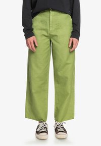 Gröna vida byxor i bomull med en mjuk textur. Har framfickor och är kombinerade med mörka sneakers.