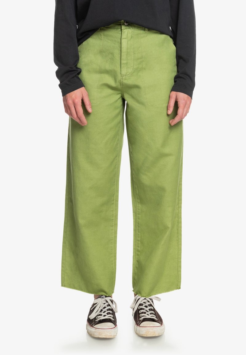 Gröna vida byxor i bomull med en mjuk textur. Har framfickor och är kombinerade med mörka sneakers.