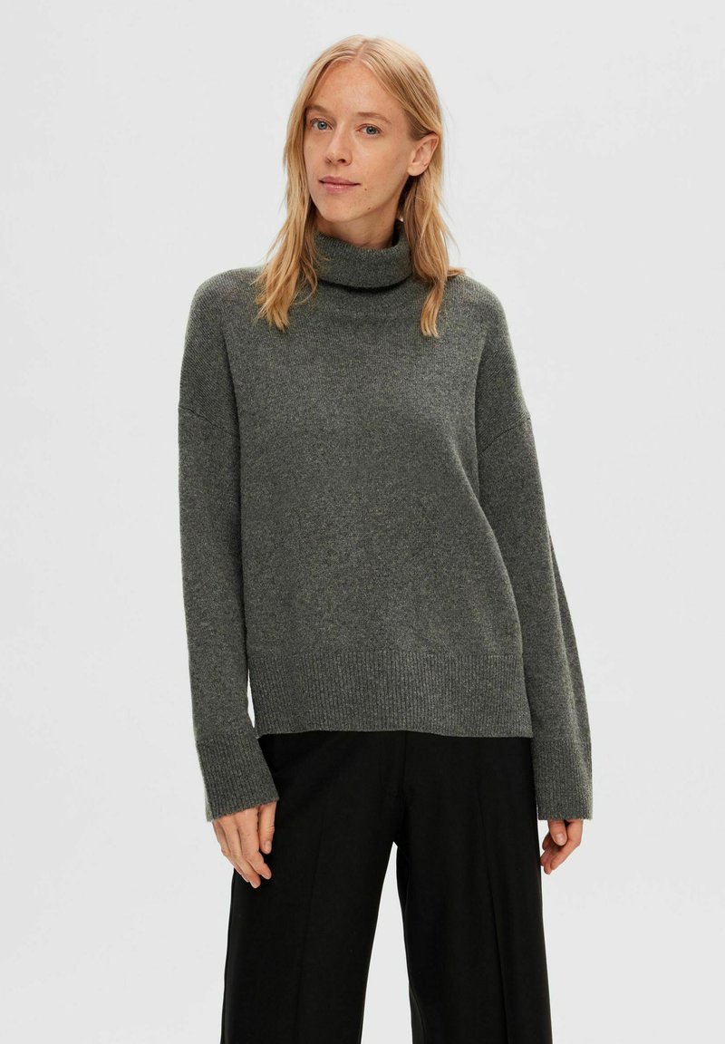 Grauer Rollkragenpullover aus weichem Strickstoff, mit einem lockeren Schnitt, gerippten Bündchen und Saum, getragen mit schwarzen weit geschnittenen Hosen.
