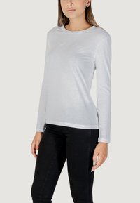 Camicia bianca a maniche lunghe realizzata in tessuto leggero, con scollatura tonda e un sottile dettaglio ricamato sul davanti.