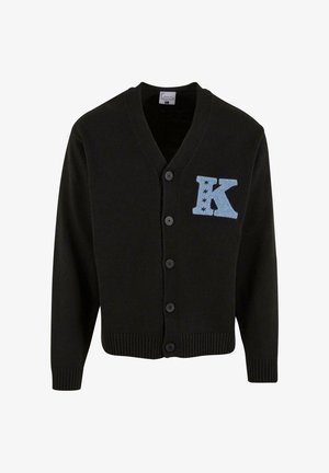 Cardigan negru din țesătură tricotată, cu decolteu în V, cinci nasturi și un "K" brodat de culoare albastru deschis cu accente de stea pe partea stângă a pieptului.
