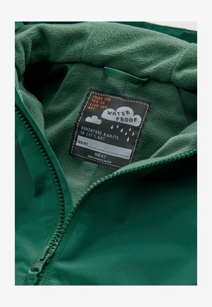 Wodoodporna zielona kurtka ma miękką fleecową podszewkę oraz czarną metkę z białym i pomarańczowym tekstem. Zamek błyskawiczny.