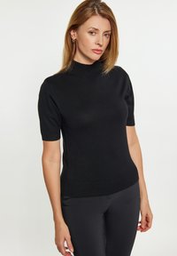 Top negru cu manșete scurte și guler înalt, având un design ajustat și o textură netedă. Purtați cu pantaloni negri ajustați.