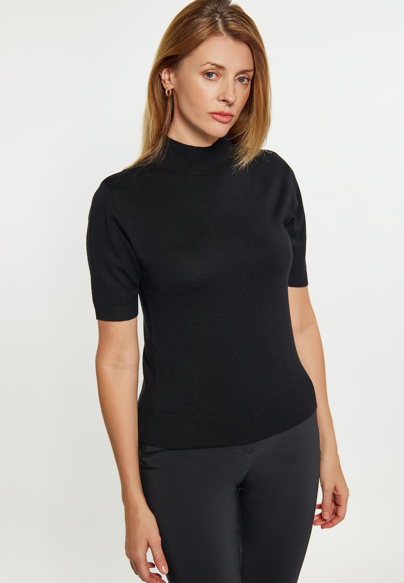 Top negru cu manșete scurte și guler înalt, având un design ajustat și o textură netedă. Purtați cu pantaloni negri ajustați.