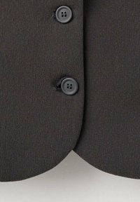 Tessuto nero con una finitura liscia e testurizzata, che presenta due bottoni neri all'collo e un dettaglio dell'orlo curvato.