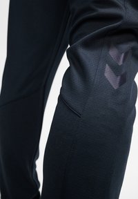Marine-blauwe sportbroek met een structuurstof, voorzien van donkere geometrische accenten op de dijen en een strakke pasvorm rond het been.