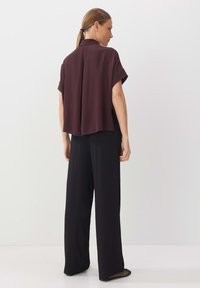 Burgundy short-sleeve blouse with a flowy design, paired with black wide-leg trousers and flat, textured shoes. Smooth fabric, relaxed fit.