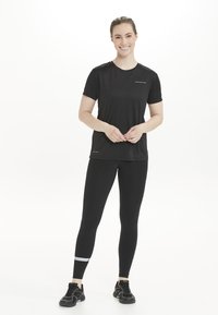 Schwarzes sportliches T-Shirt und Leggings aus feuchtigkeitsableitendem Material. Die Leggings verfügen über einen reflektierenden Akzent am Unterschenkel. Schwarze Sneaker.