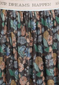 Elastyczny pasek w talii z napisem "TWOJE MARZENIA SIĘ SPEŁNIAJĄ" nad tkaniną w kwiatowy wzór w odcieniach zieleni, niebieskiego, pomarańczowego i żółtego.